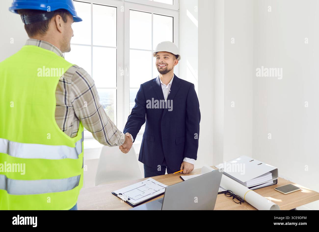 Architect with engineer reaching agreement and shaking hands discussing construction blueprint Stock Photo