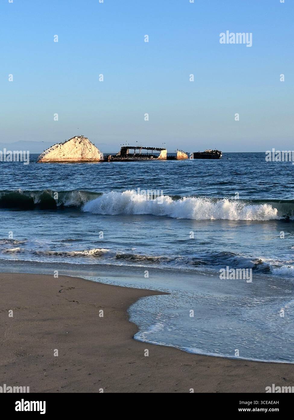 The partially submerged concrete shipwreck SS Palo Alto sits off Seacliff State Beach in Aptos, California, with waves breaking along the sandy shorel - Smartphone Captured Stock Image