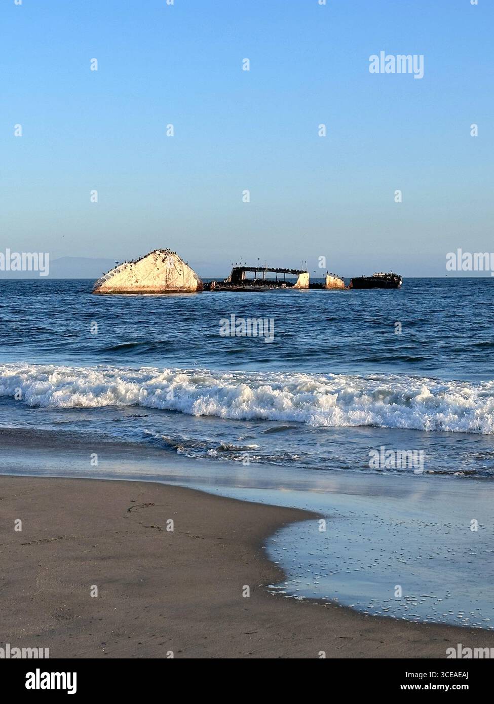 The partially submerged concrete shipwreck SS Palo Alto sits off Seacliff State Beach in Aptos, California, with waves breaking along the sandy shorel - Smartphone Captured Stock Image