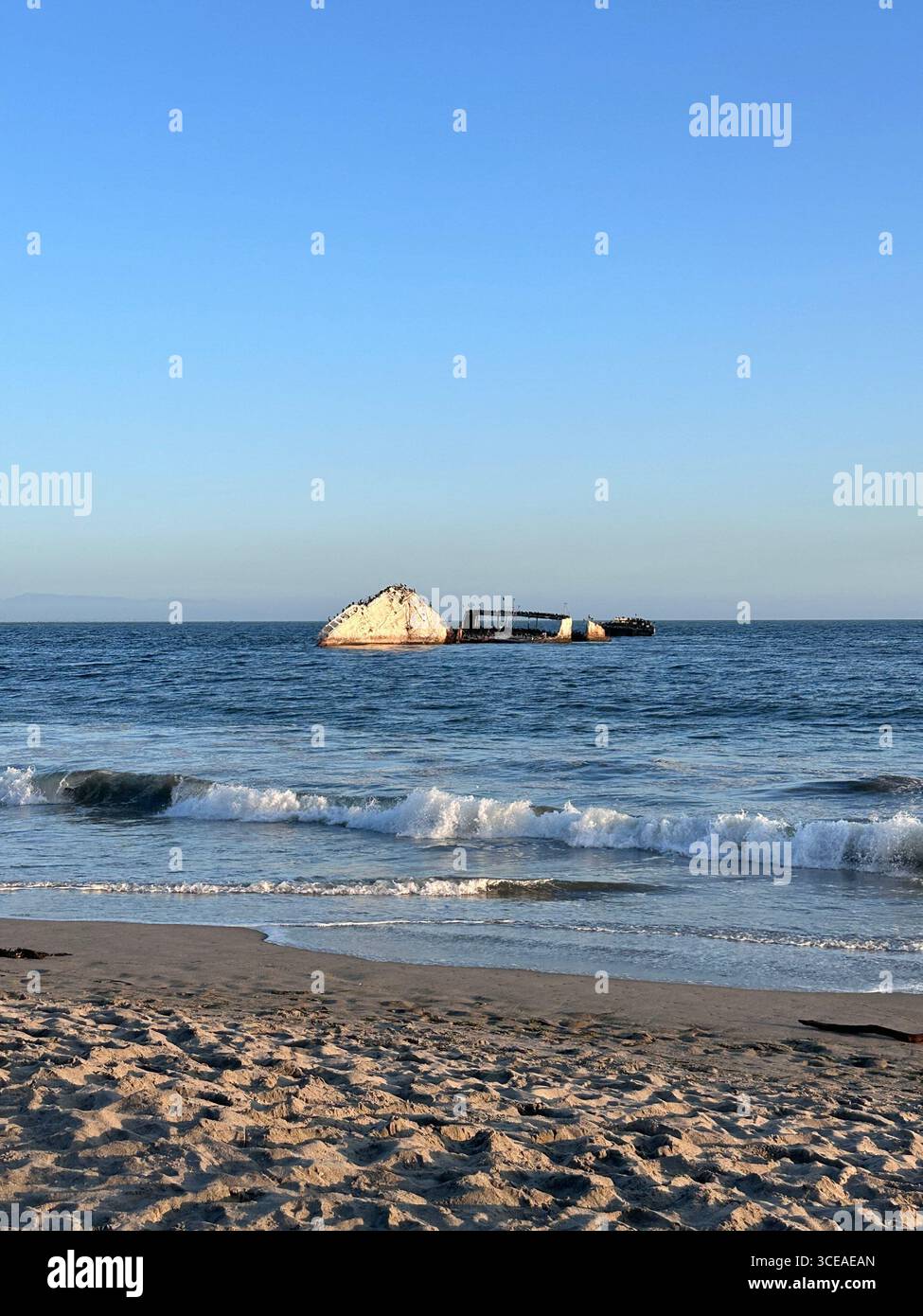 The partially submerged concrete shipwreck SS Palo Alto sits off Seacliff State Beach in Aptos, California, with waves breaking along the sandy shorel - Smartphone Captured Stock Image