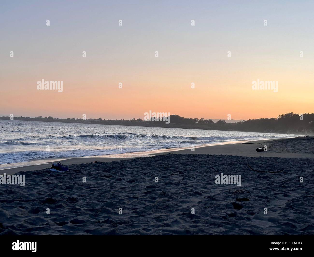 A peaceful ocean sunset with gentle waves washing onto the sandy beach, creating a reflective glow of orange and purple hues in the water and sky. - Smartphone Captured Stock Image