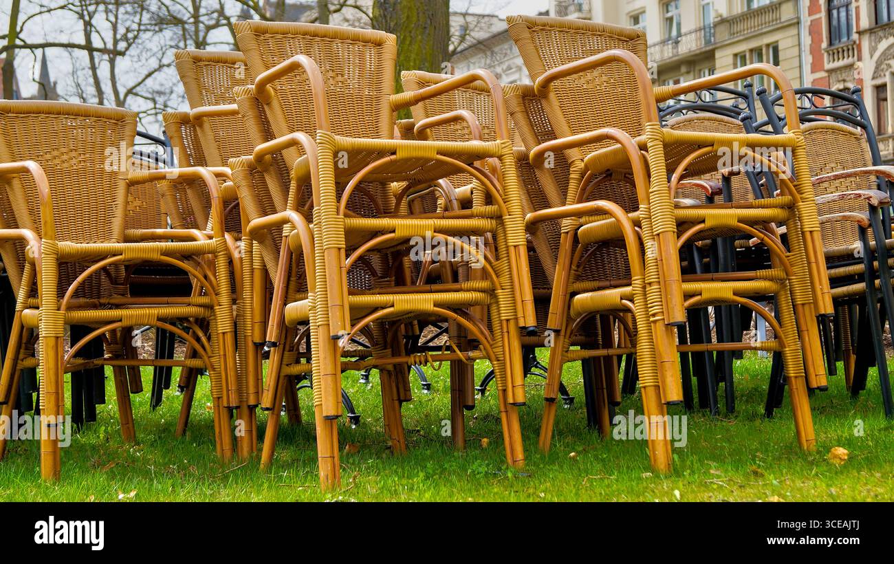 Stacked wicker chairs on a lawn – outdoor seating stored on the grass in a natural setting. Stock Photo