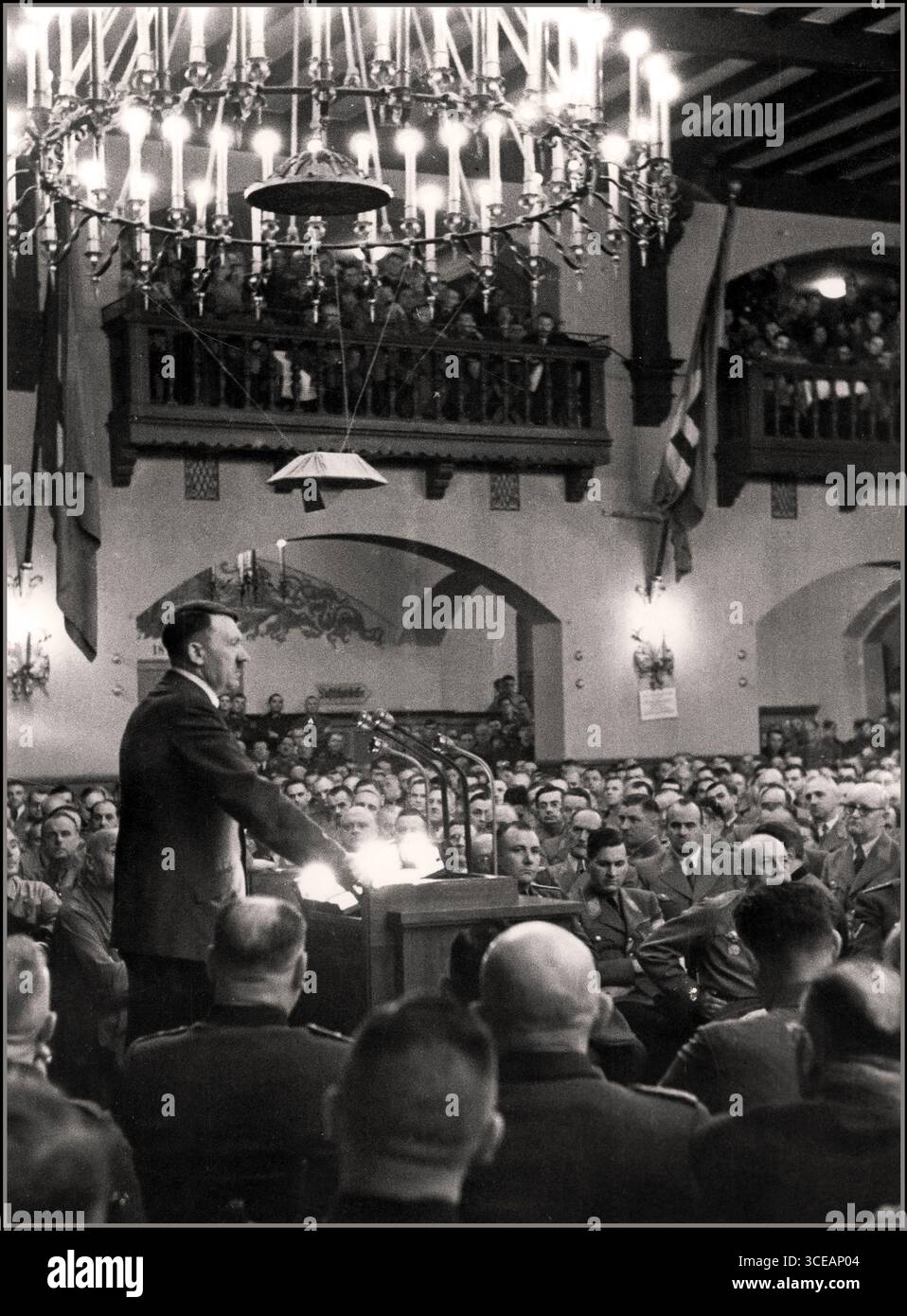 “Adolf Hitler delivering a speech at the Löwenbräukeller beer hall in Munich during the annual commemoration of the failed Beer Hall Putsch, 8 November 1941. The Putsch of 1923, in which Hitler and the early National Socialist movement attempted to seize power, had become a central ritual in the Nazi calendar, marked each year with speeches, parades, and memorial ceremonies. The Löwenbräukeller, together with the nearby Bürgerbräukeller, served as key venues for these commemorations. The 1941 event occurred shortly after the launch of Operation Barbarossa. Stock Photo