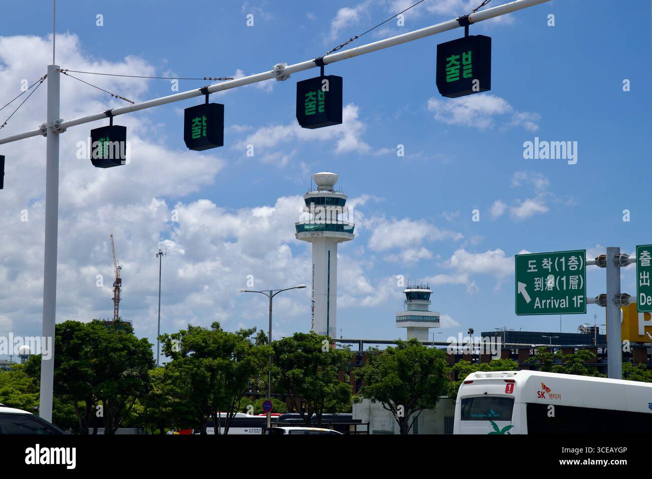 Jeju International Airport’s control towers rise beyond roadside trees ...