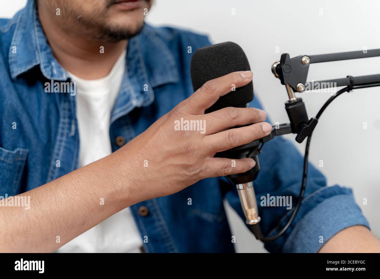 Focused young man speaking into a microphone while recording a podcast in a professional studio environment. Stock Photo
