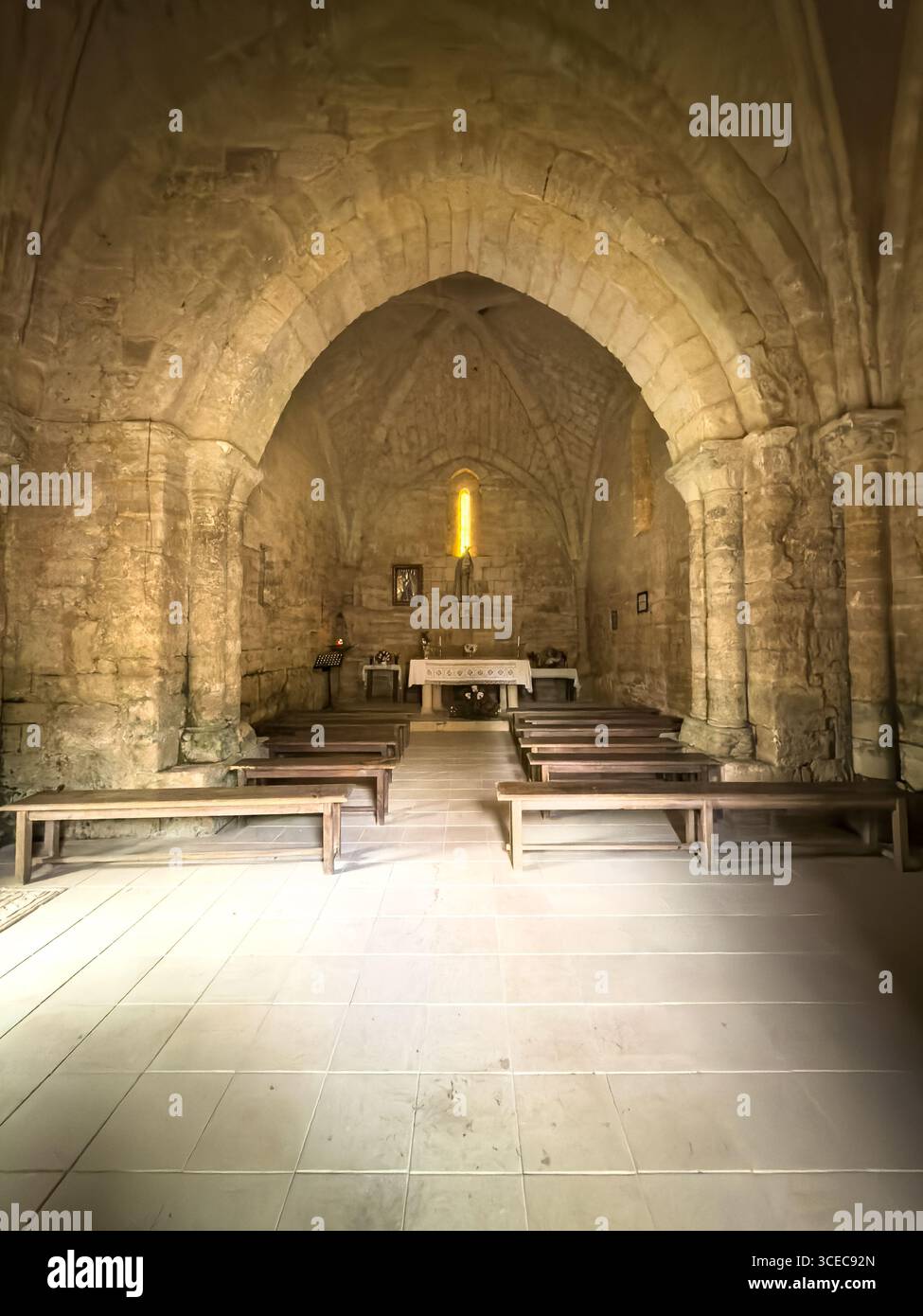 Simple Romanesque altar with flowers, statue and stone vault inside