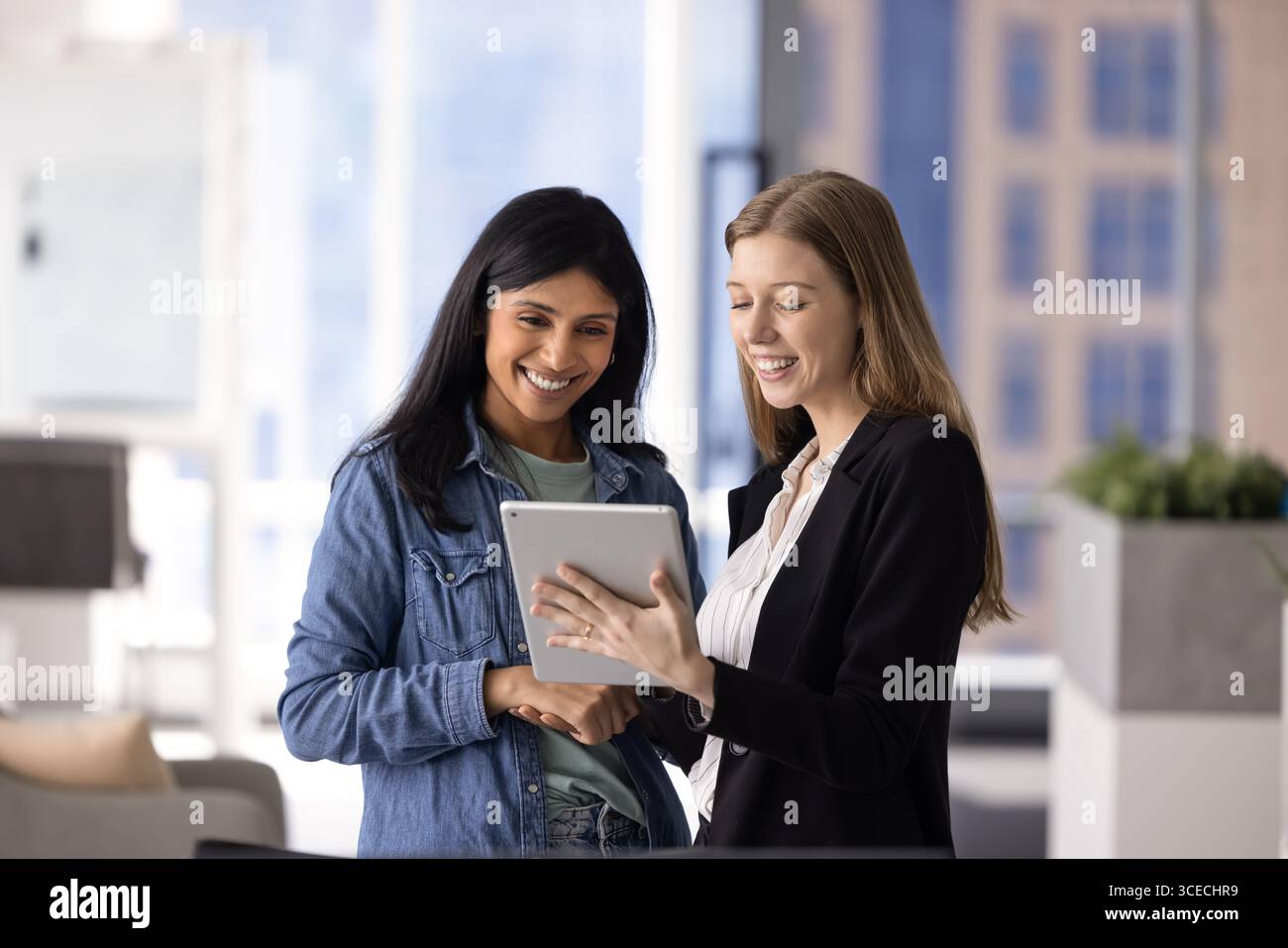 Two happy multiethnic female coworkers using digital technology Stock Photo