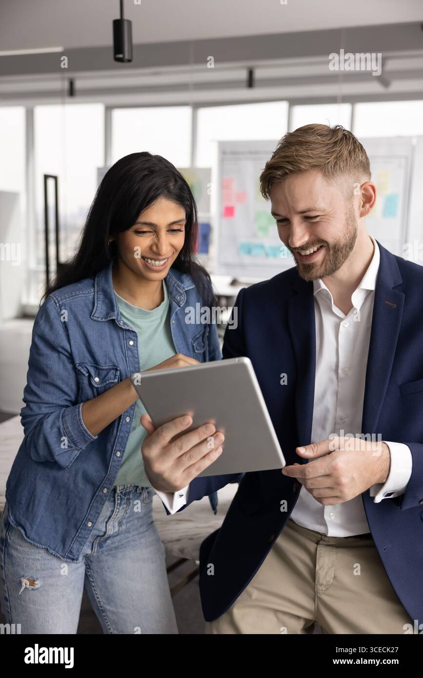 Two positive young diverse colleagues using digital tablet together Stock Photo