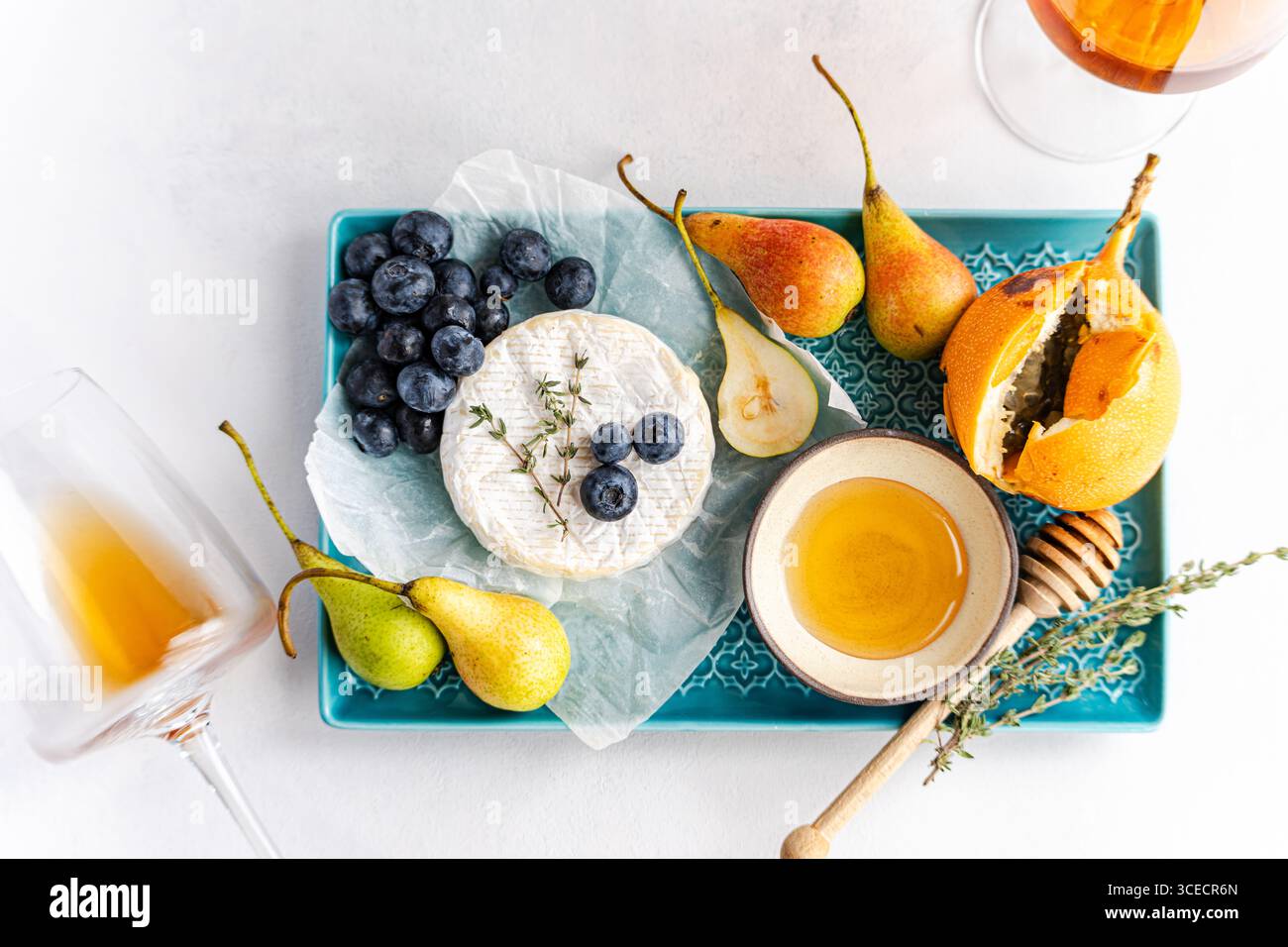 A beautifully arranged gourmet platter featuring creamy brie cheese, fresh blueberries, sliced pears, and a drizzle of honey on a decorative tray, acc Stock Photo
