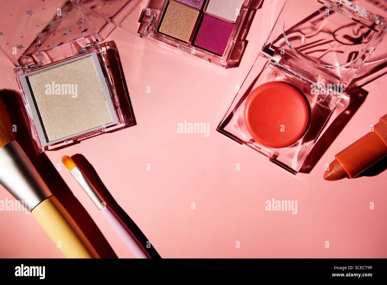 Top view of vibrant pink makeup set, including eyeshadow palette, blush, lipstick, and brushes, arranged on a pastel pink surface. Acrylic cases refle Stock Photo