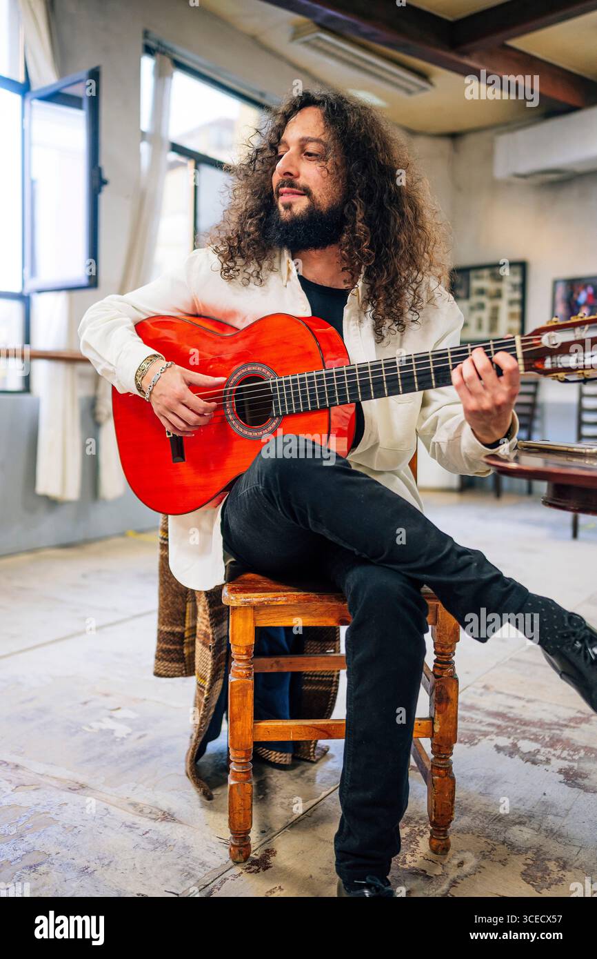 Latin man with long hair playing red bass guitar in studio Stock Photo