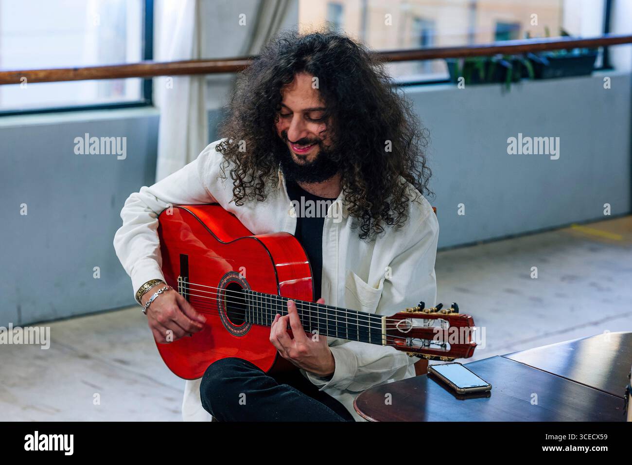 Latin man with long hair playing red bass guitar in studio Stock Photo