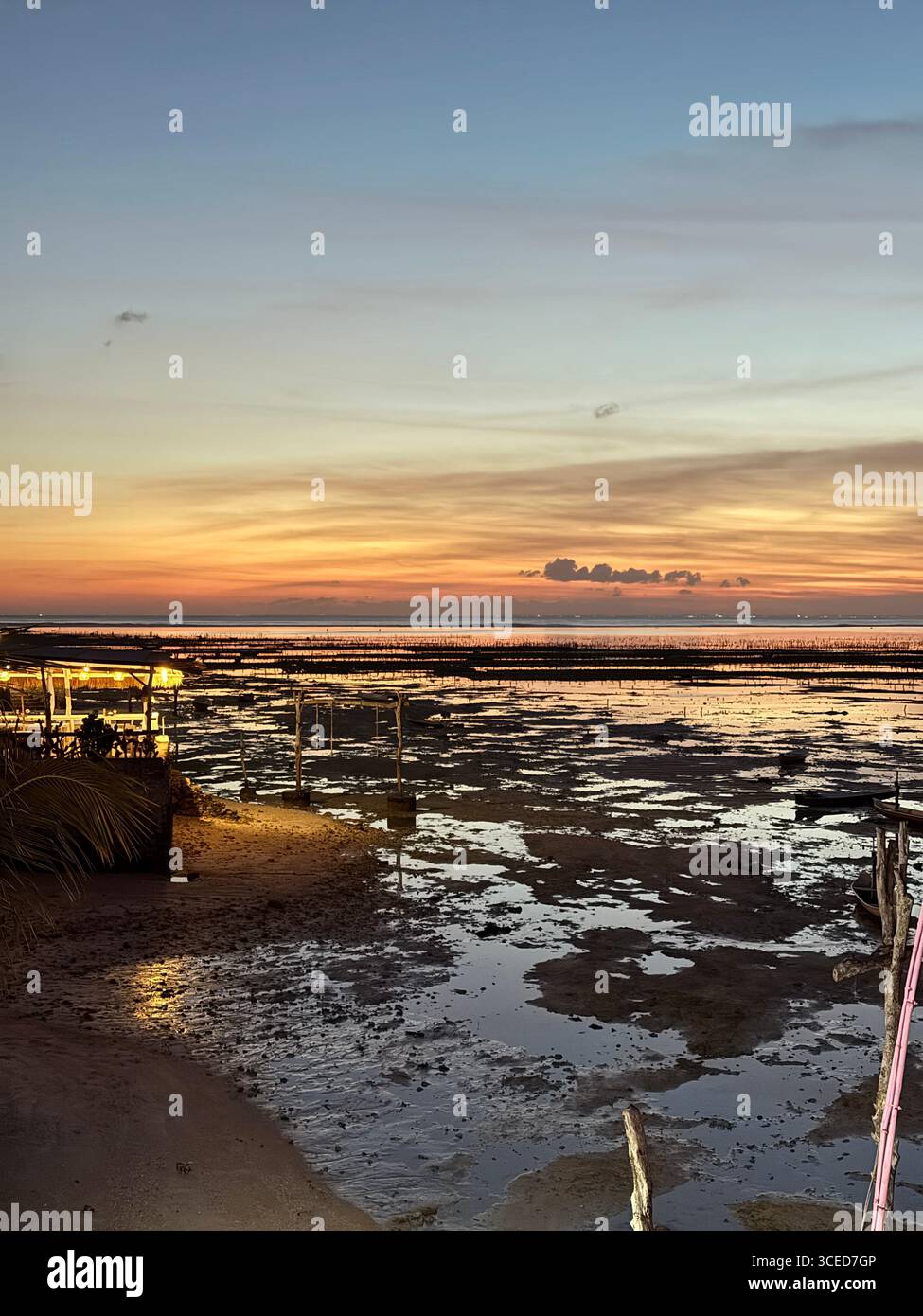 Golden tropical sunset over coastline in Nusa Lembongan, Bali, Indonesia, with tidal pools and calm ocean horizon reflecting warm evening colors in sky. - Smartphone Captured Stock Image