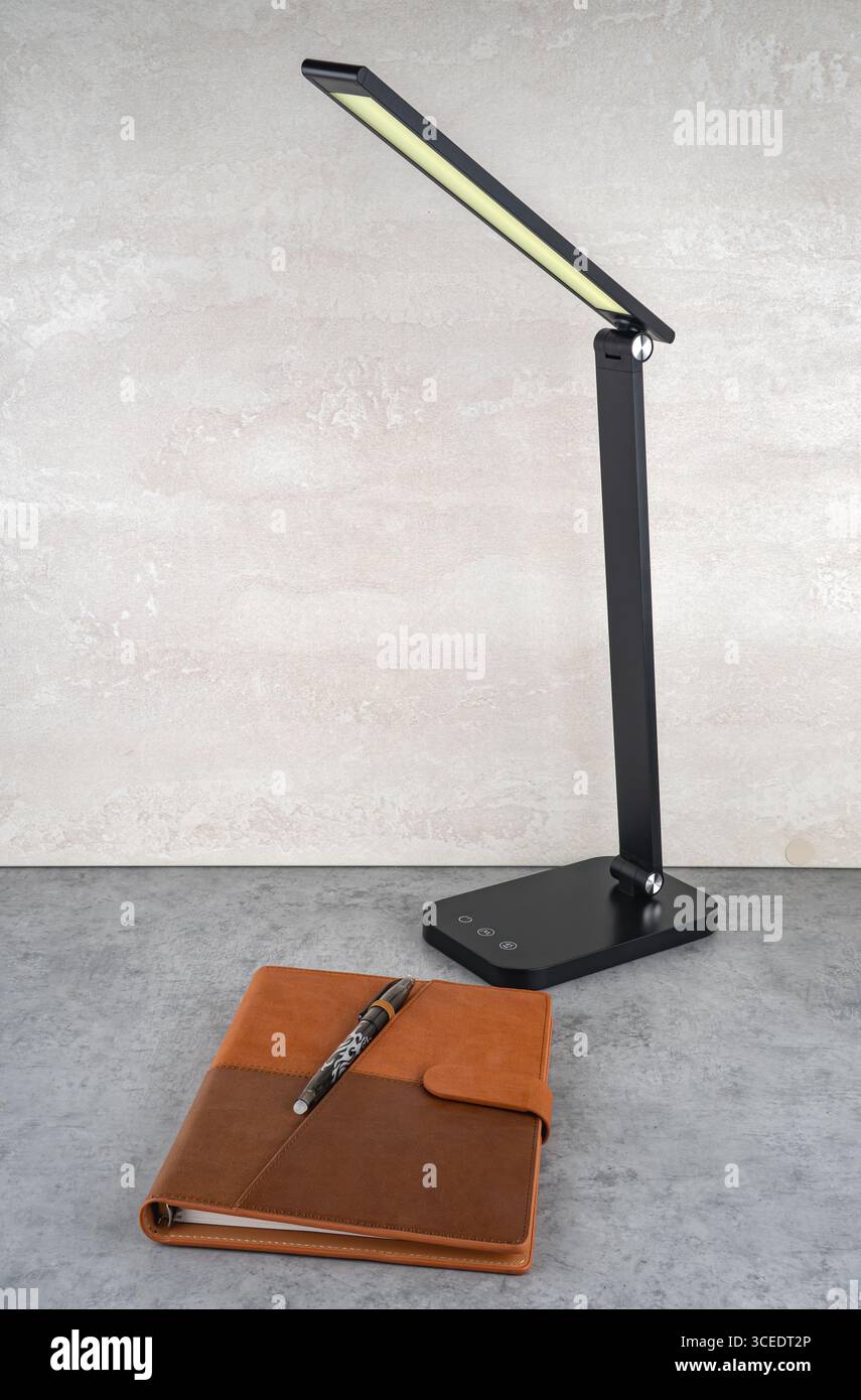 A modern design table lamp emits soft light onto the table and notebook. Stock Photo