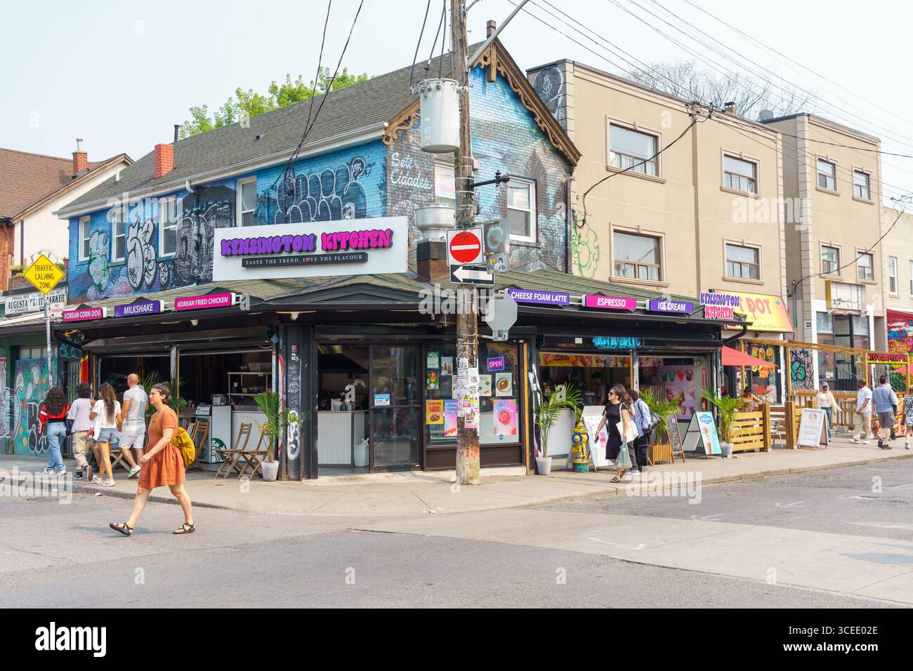 People walk past Kensington Kitchen, a colorful corner eatery with graffiti-covered walls in Kensington Market. Stock Photo