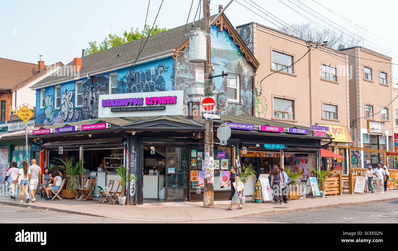 People pass by Kensington Kitchen, a vibrant eatery with graffiti walls and bold signage in Kensington Market. Stock Photo