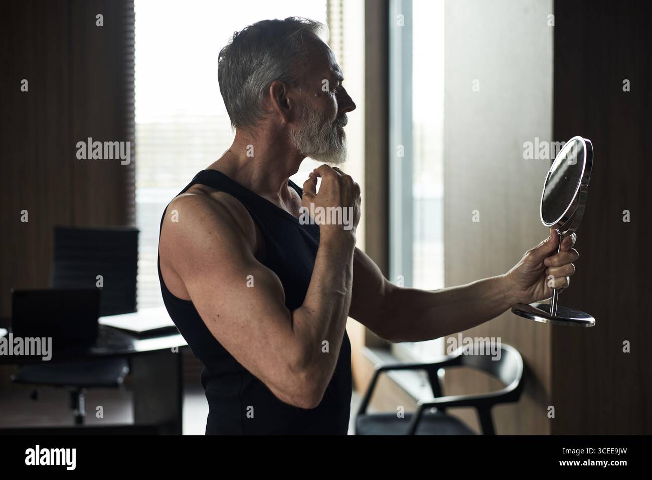 Middle Aged Caucasian Man Grooming Beard While Looking into Handheld Mirror Stock Photo