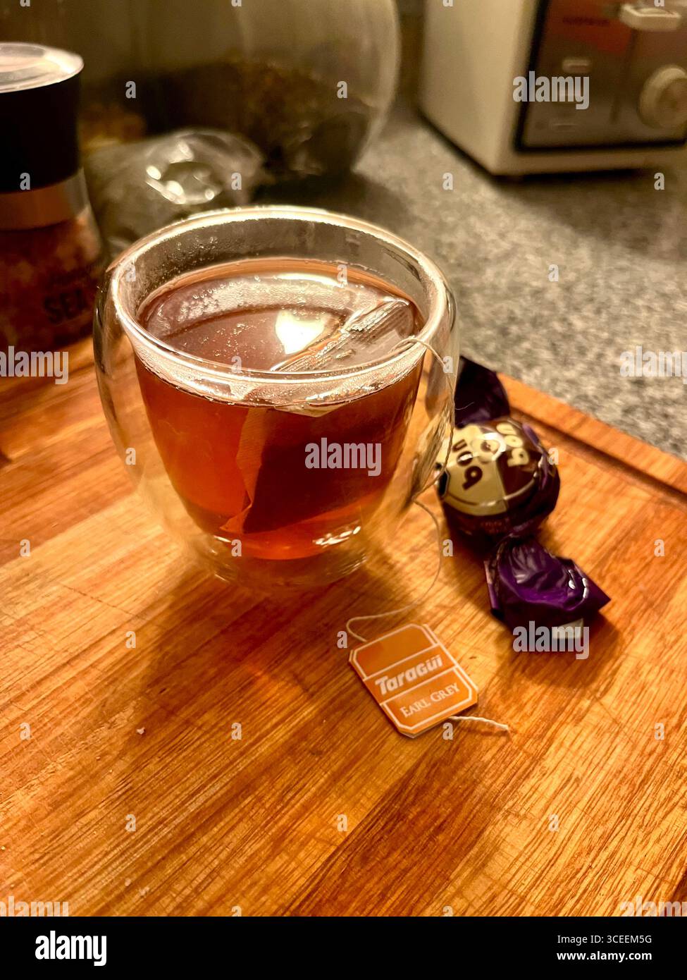 A cold beverage served in a clear glass jar with a paper straw and fruit garnish on a wooden table. - Smartphone Captured Stock Image