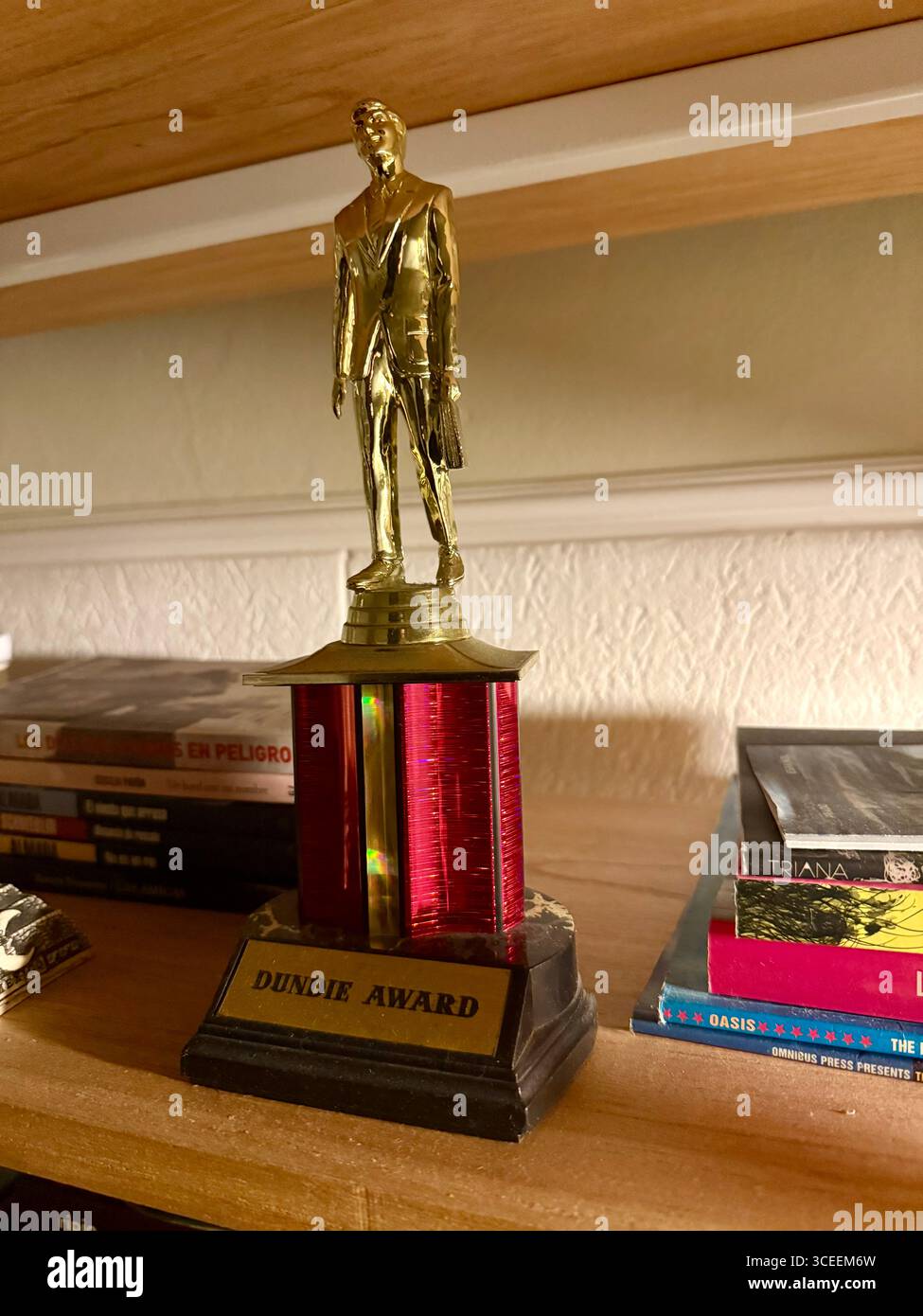 A gleaming gold trophy in the shape of a standing human figure on a red wooden base, displayed on a table, symbolizing achievement and excellence. - Smartphone Captured Stock Image