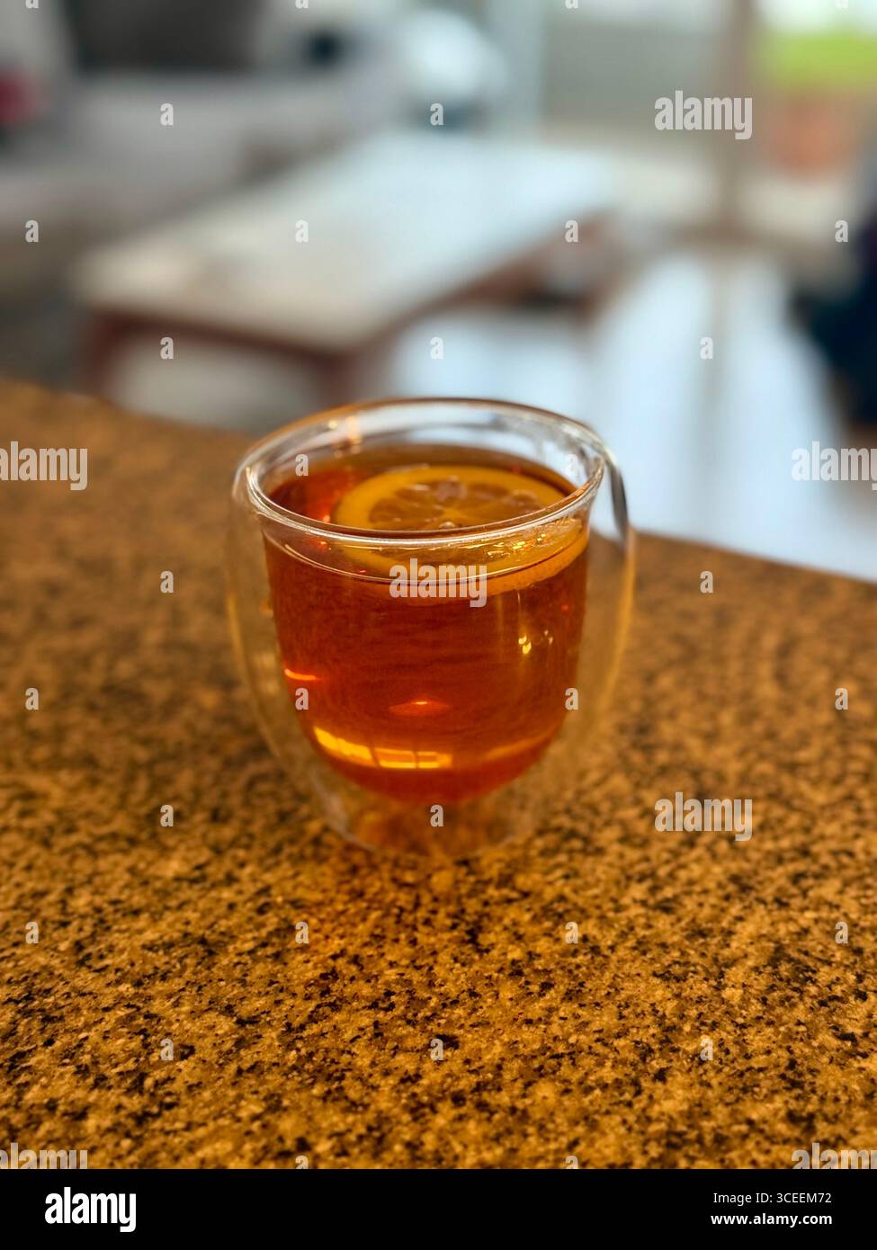 A small glass of amber-colored beverage served on a wooden table, with a blurred restaurant background. - Smartphone Captured Stock Image
