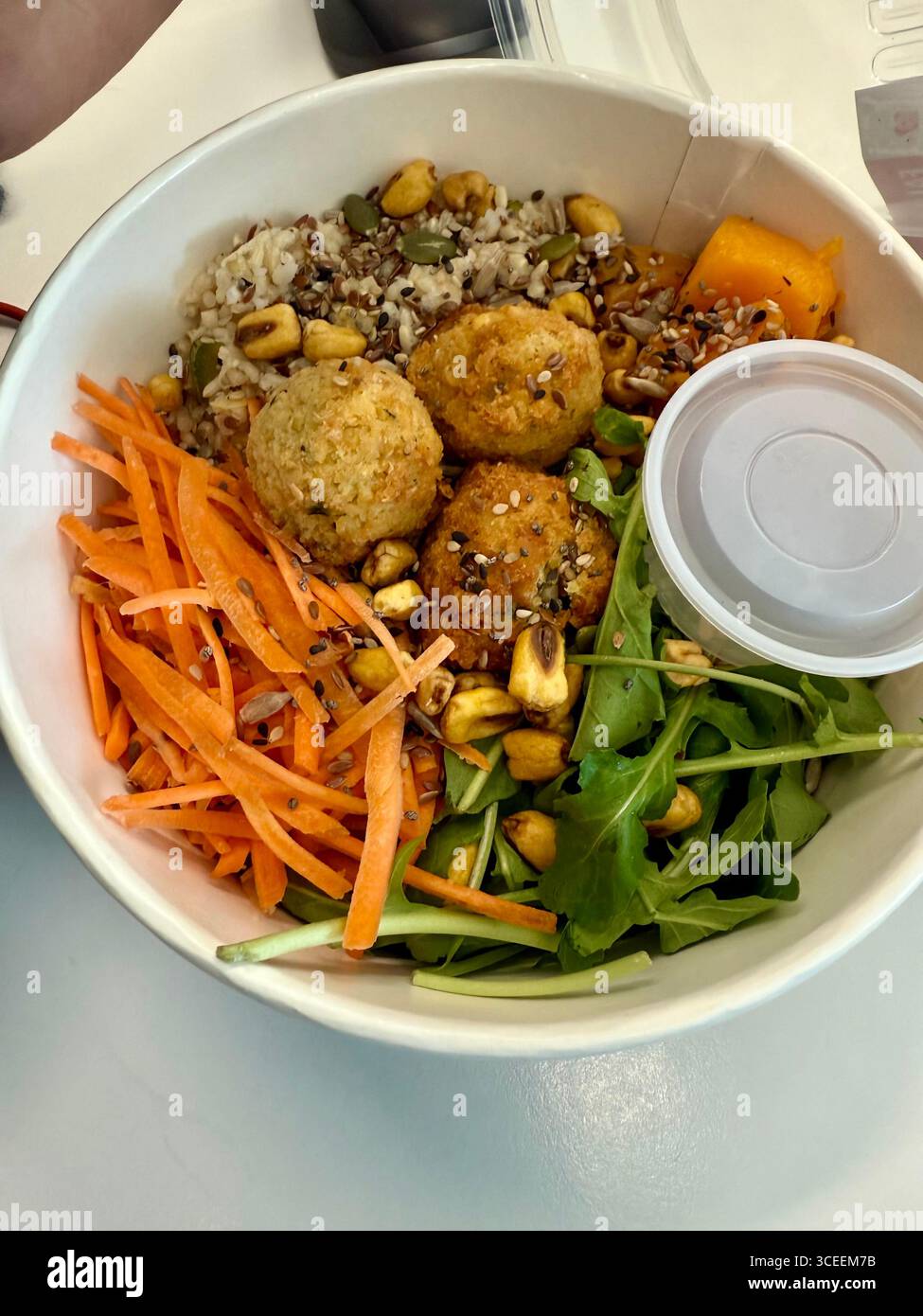 A colourful salad bowl filled with mixed greens, shredded carrots, chickpeas, beans, grains, and falafel balls, served with a small dressing container - Smartphone Captured Stock Image