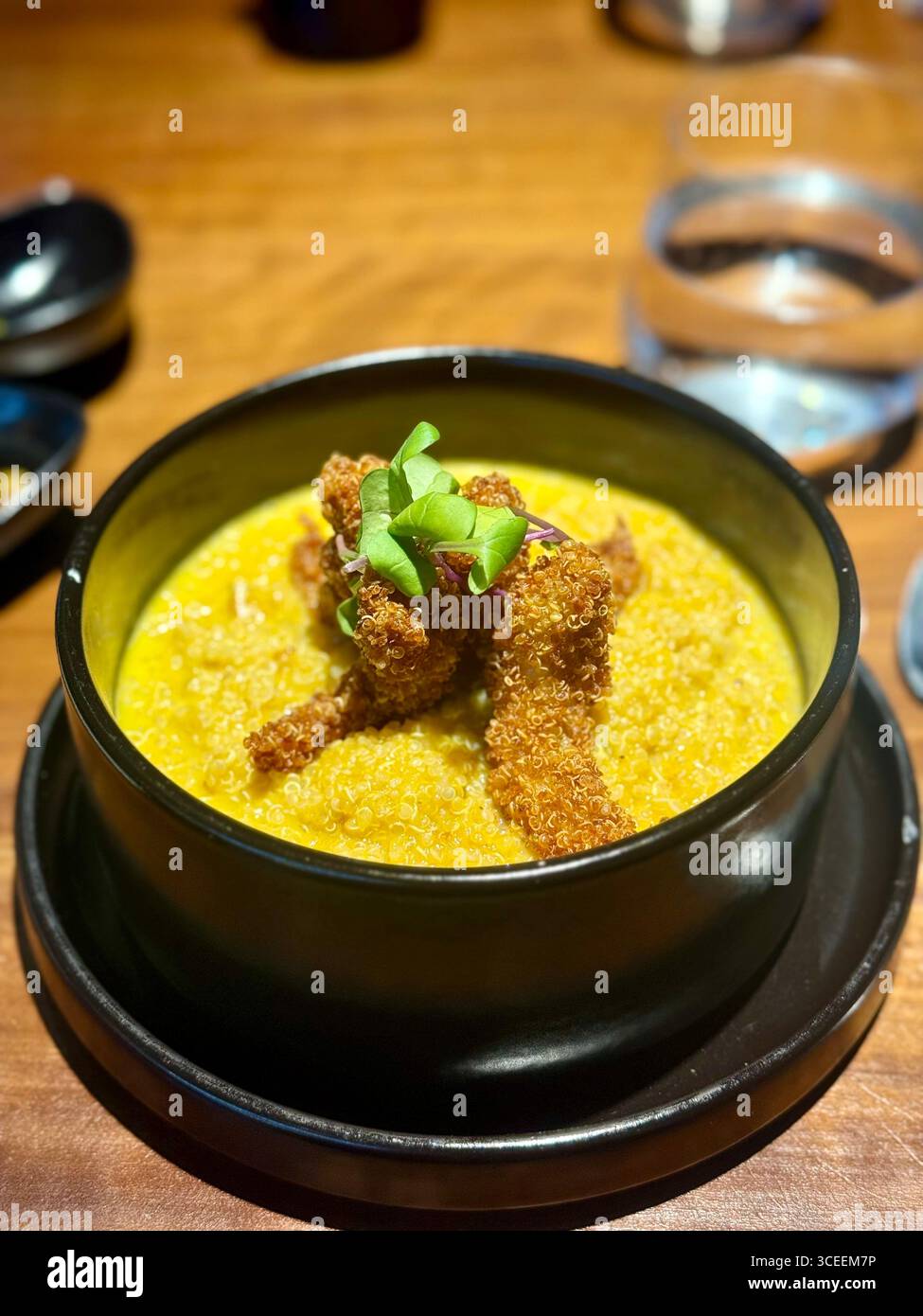 A steaming bowl of creamy yellow curry garnished with green herbs, served in a black stone pot on a restaurant table. - Smartphone Captured Stock Image