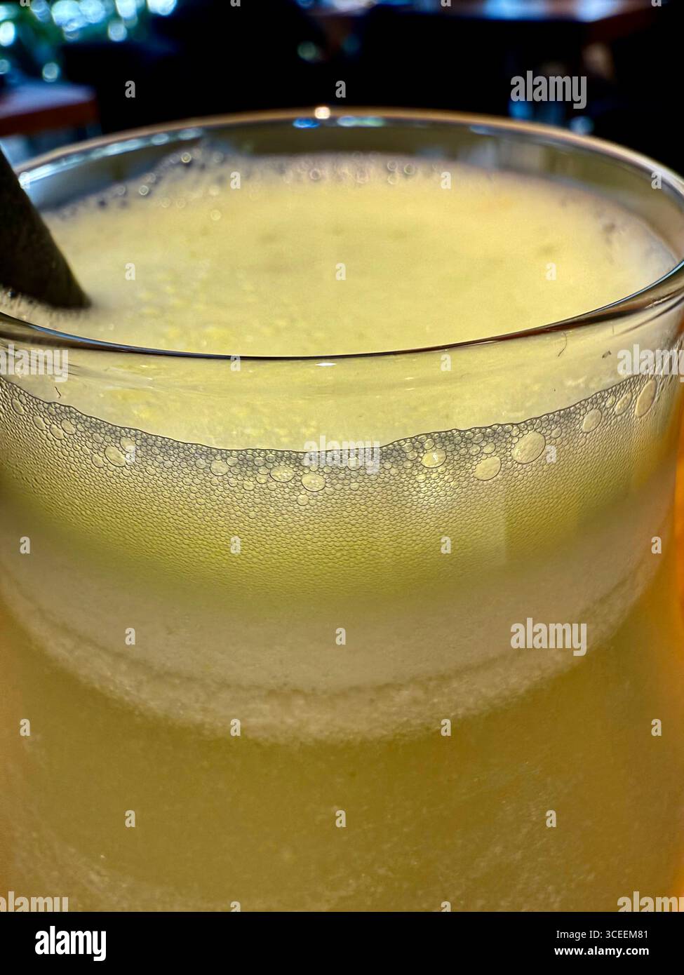 A pale yellow frothy beverage served in a glass on a table at a restaurant, refreshing and chilled. - Smartphone Captured Stock Image