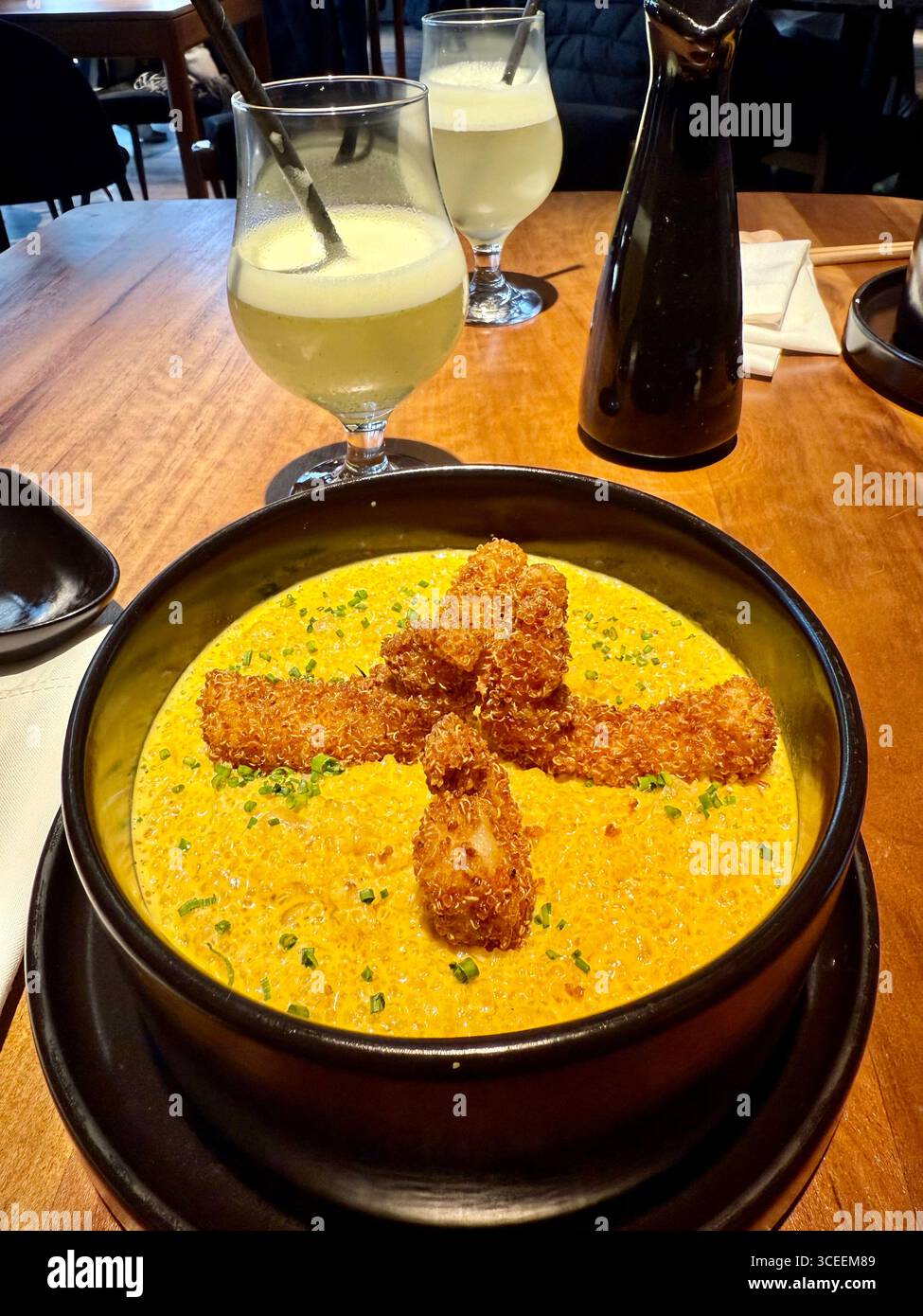 A dish of creamy yellow risotto topped with crispy breaded shrimp pieces arranged upright in a black bowl. - Smartphone Captured Stock Image