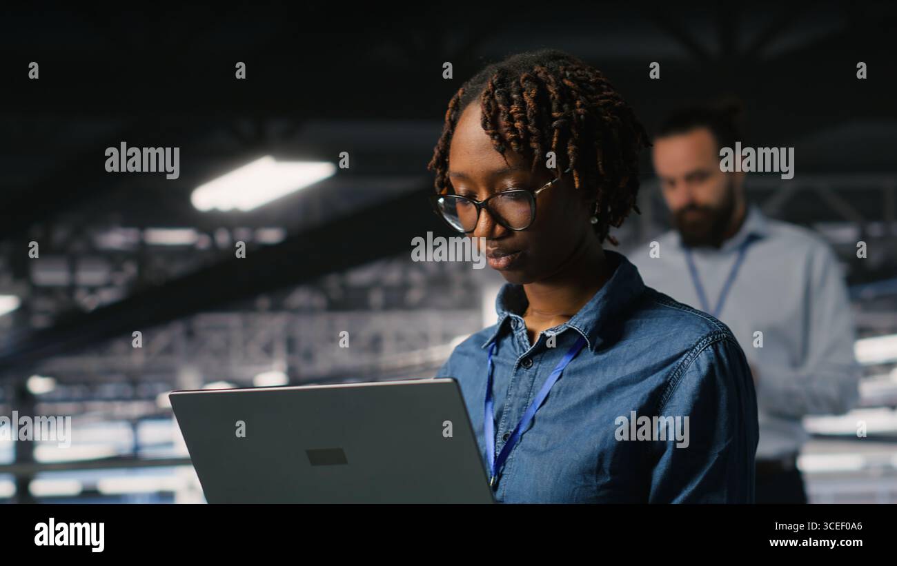 System administrators on data center industrial platform analyzing performance outputs on laptop. Server hub teamworking colleagues finetuning server rig configurations using notebook Stock Photo
