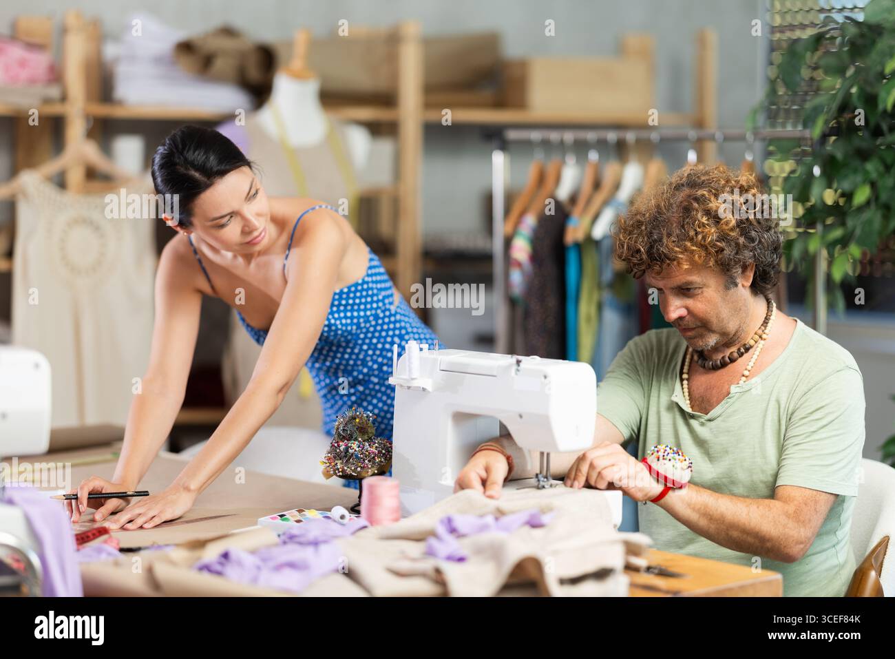 Young female dressmaker drawing with curves while man sewing Stock ...