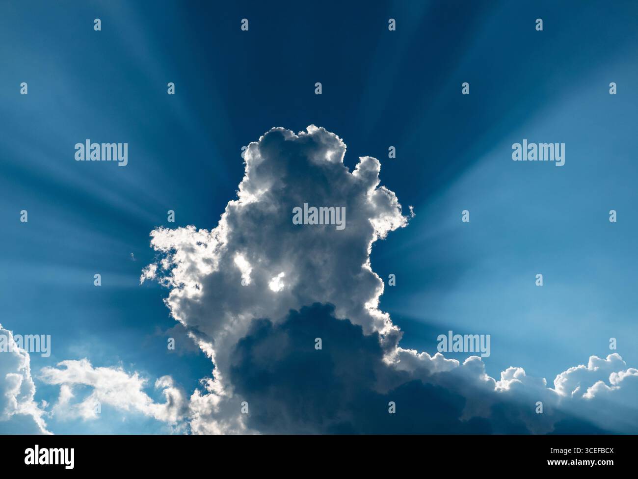 Dramatic sky with deep blue sky, backlit clouds and sunbeams. Stock Photo