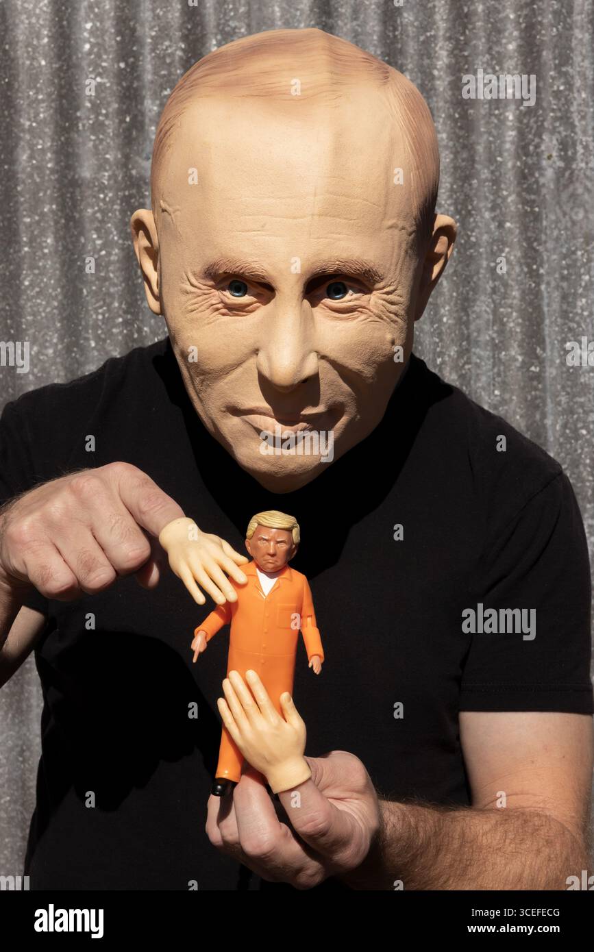 A looming Putin masked person manipulates a Trump doll in orange, symbolizing control, power, and political satire. Stock Photo