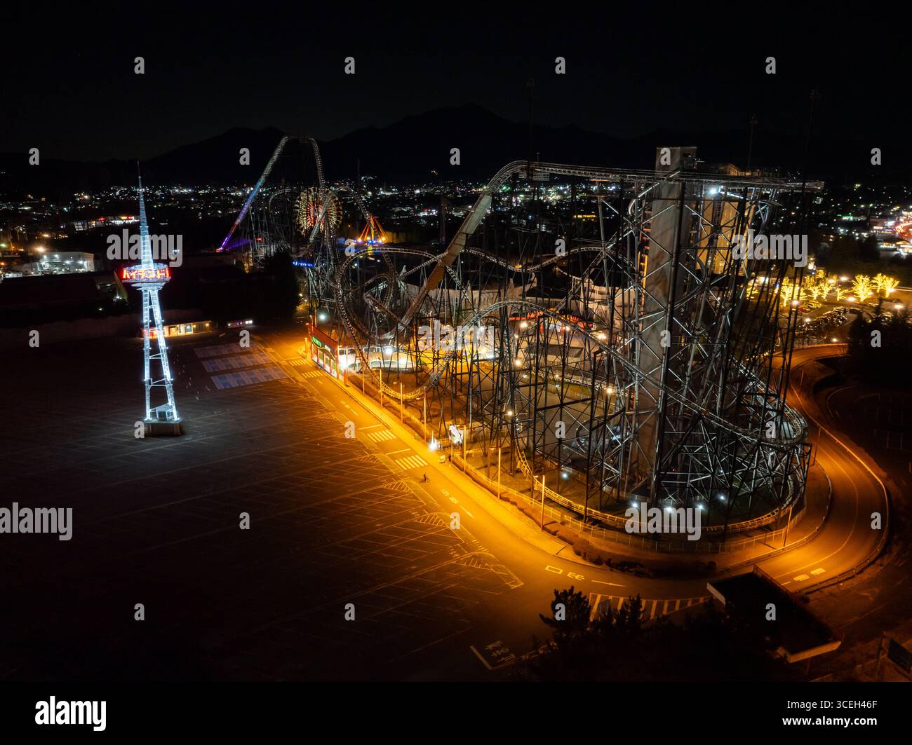 Aerial view of Fujiyama Tower and illuminated rollercoasters piercing the night sky, the city lights twinkling softly in the distance, Fujiyoshida, Ya Stock Photo