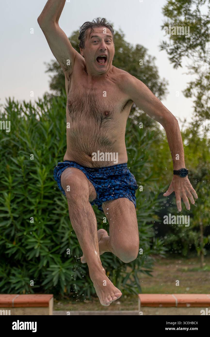 A wet man in a swimsuit jumps high into a swimming pool Stock Photo