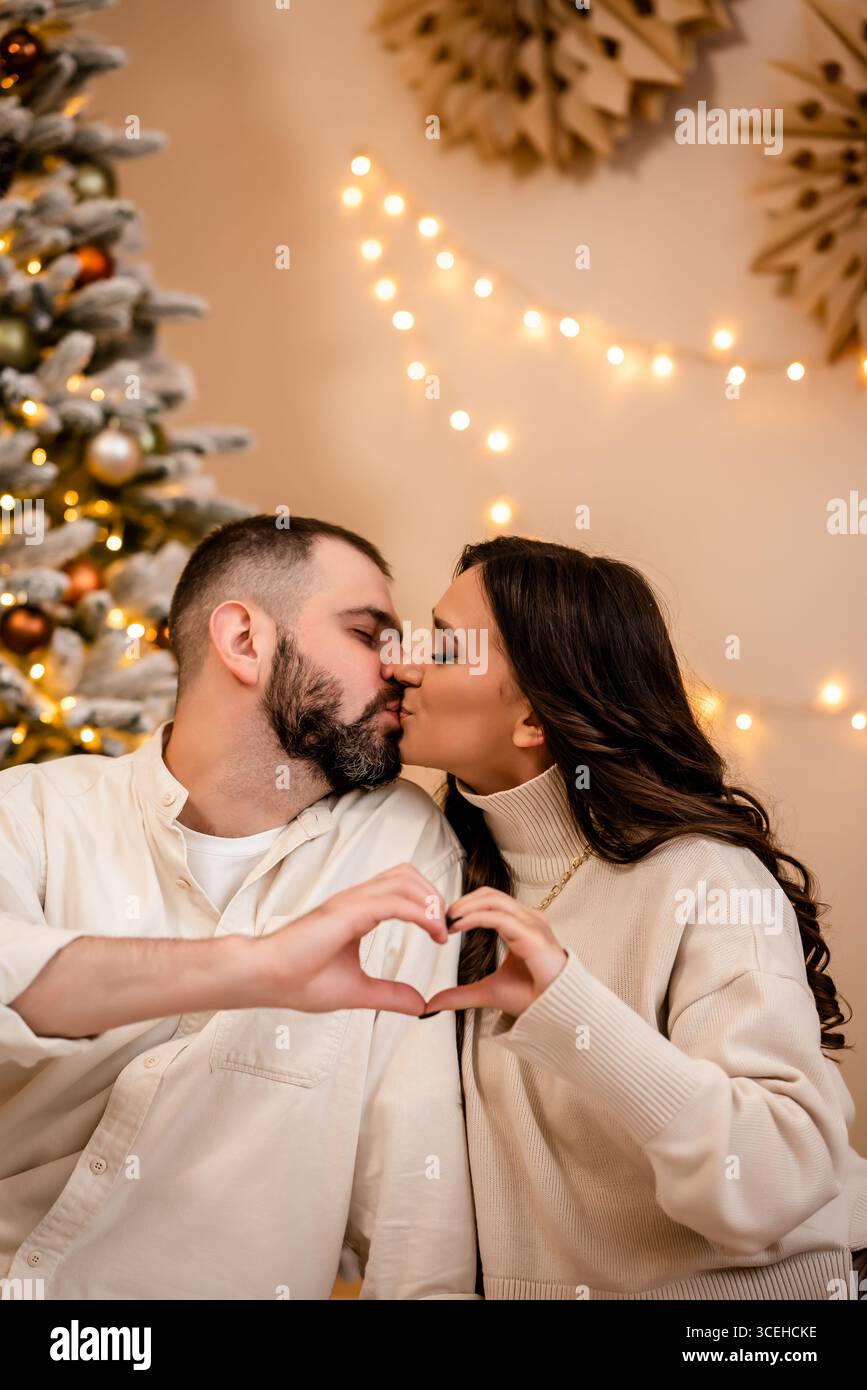 Couple Sharing a Kiss by Christmas Tree with Heart Gesture Stock Photo ...