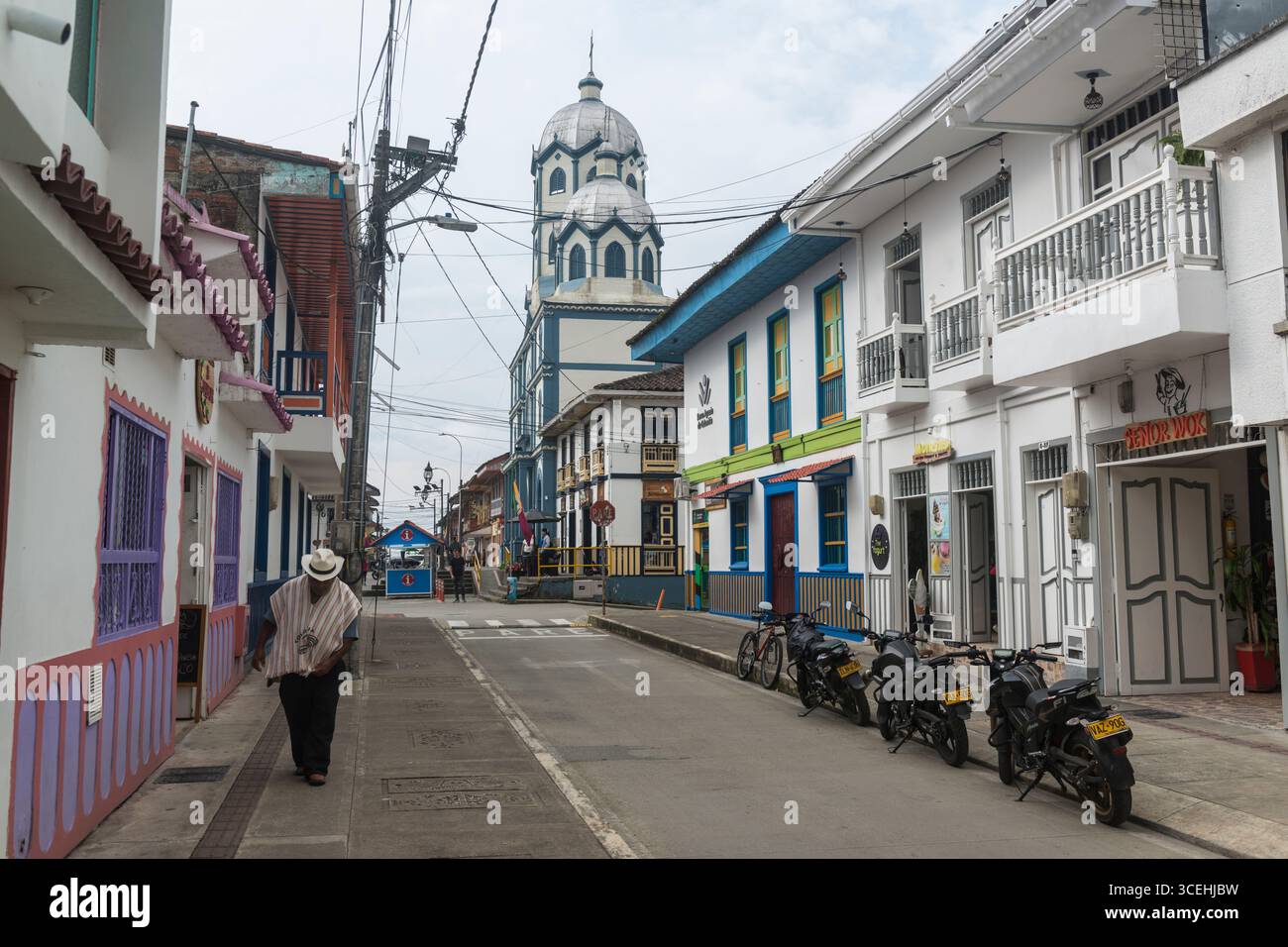Elderly man with poncho and hat walking in a street leading to the Iglesia Maria Inmaculata in Filandia, Quindío Department, Colombia Stock Photo