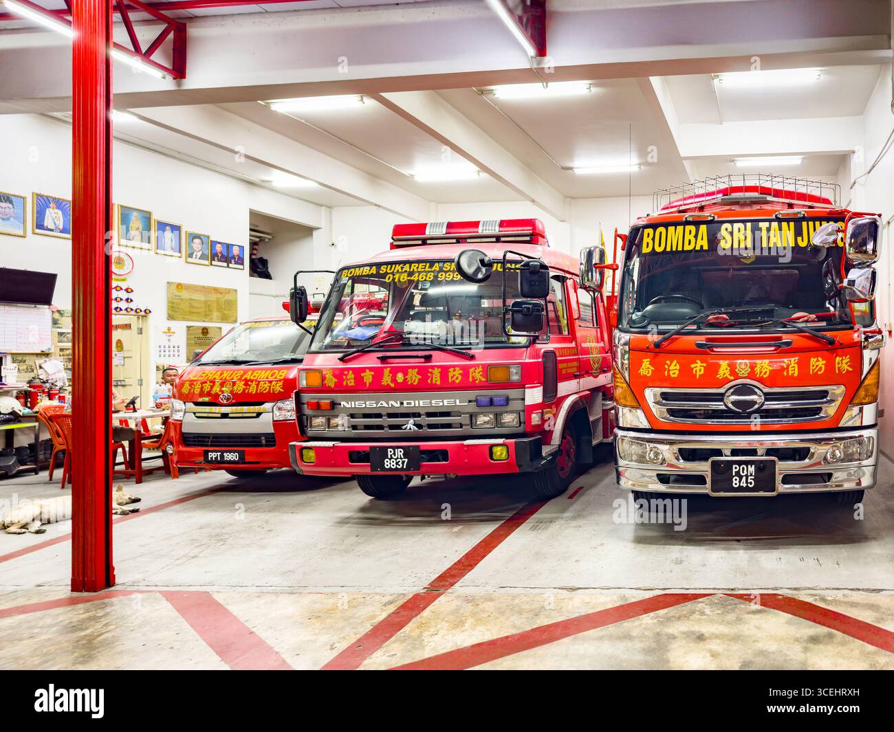 Three red fire trucks parked inside a Malaysian fire station with cultural decorations on the walls George town Penang Malaysia malaysian fire engines - Smartphone Captured Stock Image