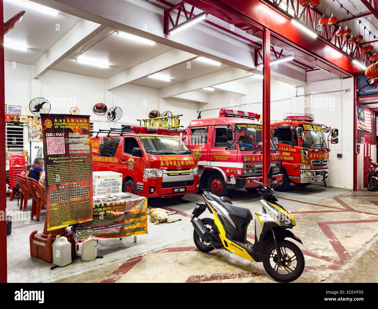 Three red fire trucks parked inside a Malaysian fire station with cultural decorations on the walls George town Penang Malaysia malaysian fire engines - Smartphone Captured Stock Image