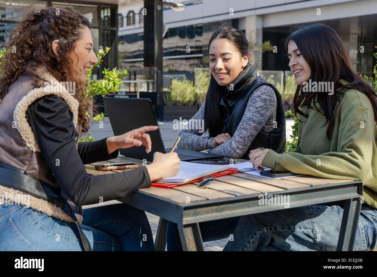 Three university students collaborating on a project, using a laptop and taking notes outdoors Stock Photo