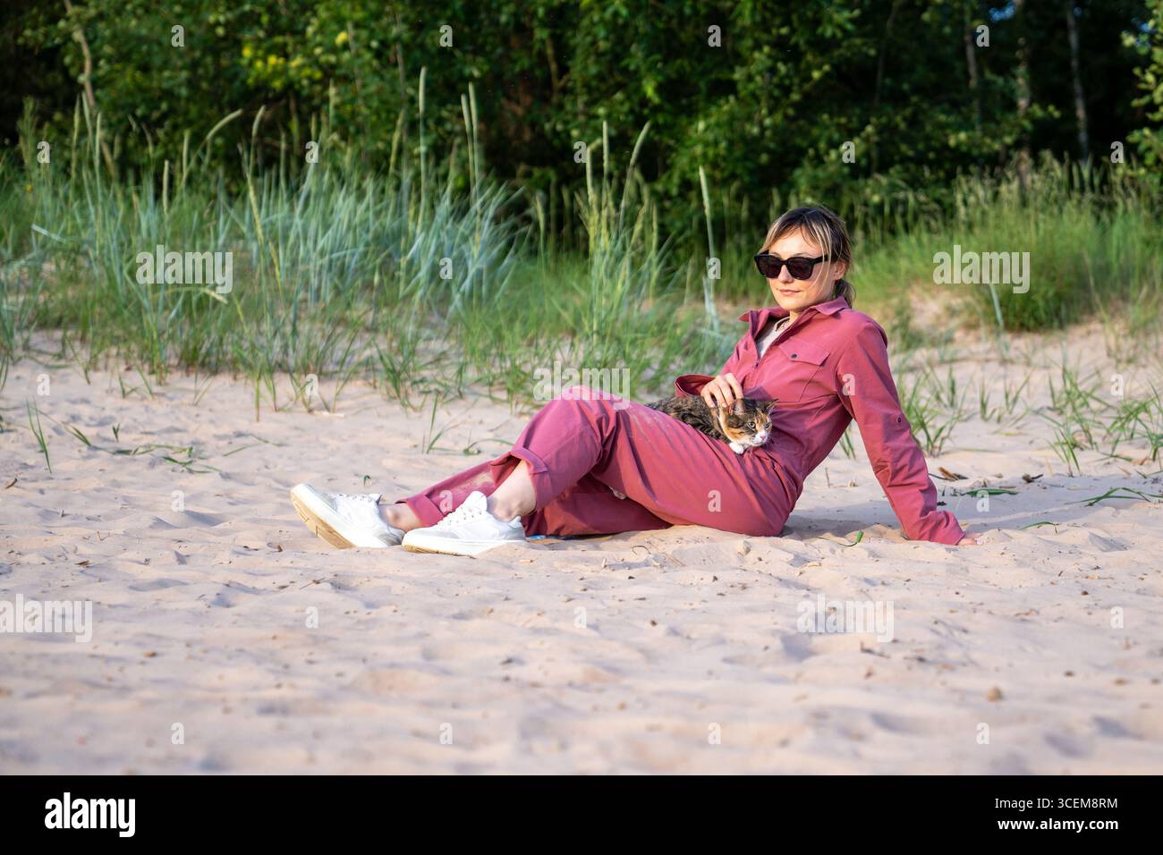 Woman relax on sandy coast stroking cat at morning walk, enjoy peaceful beach time petting feline Stock Photo