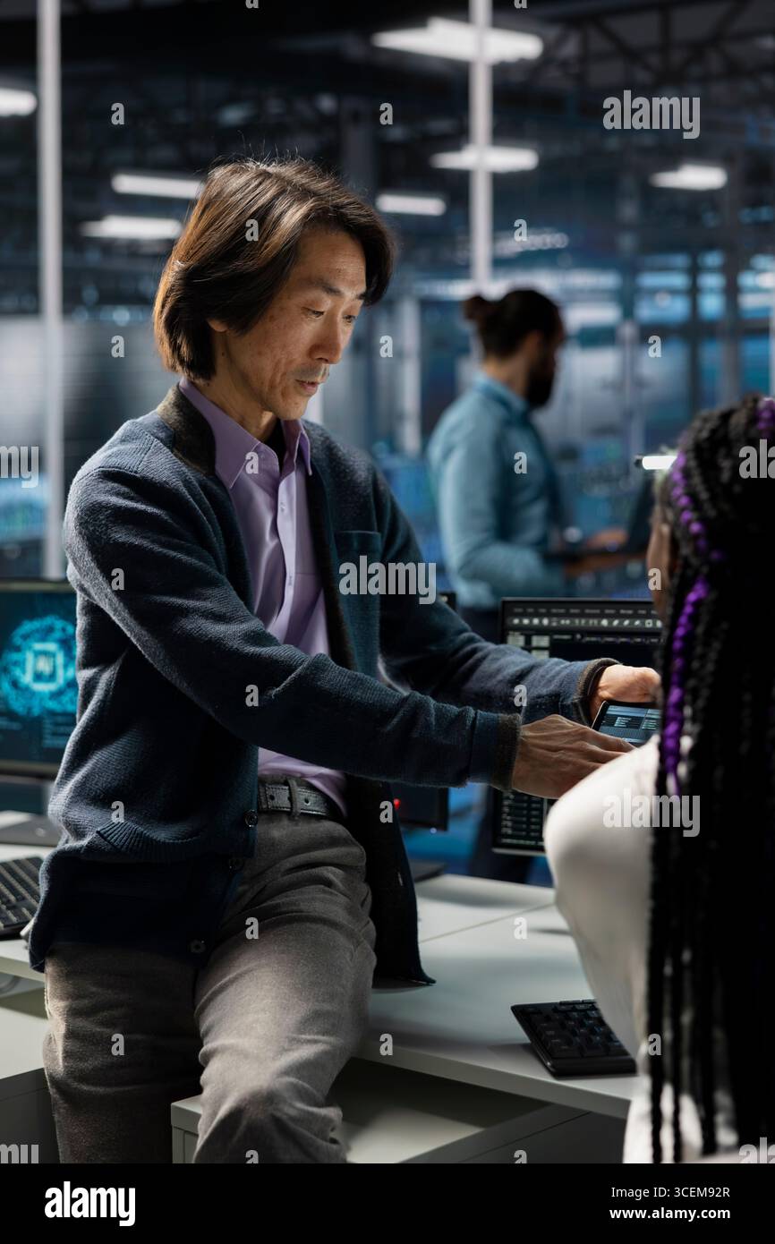 Manager and intern in data center troubleshoot server connectivity issues using AI. Senior programmer and young colleague in server room audit systems for vulnerabilities using artificial intelligence Stock Photo