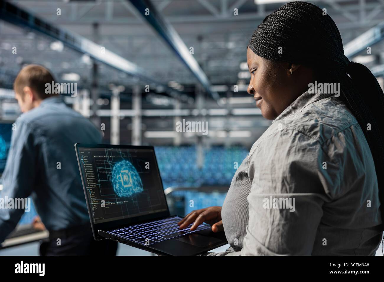 Smiling IT expert in server room using laptop to improve AI system scalability for increased workloads. Happy data center programmer using notebook to adjust artificial intelligence model parameters Stock Photo