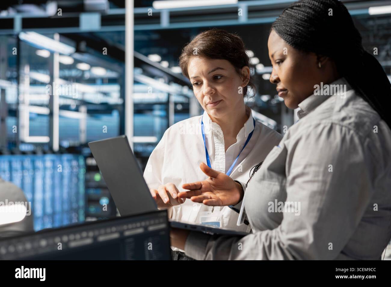 Team of system administrators in data center using laptop to update storage arrays software, configuring network virtualization. Server hub IT specialists using notebook to verify settings Stock Photo
