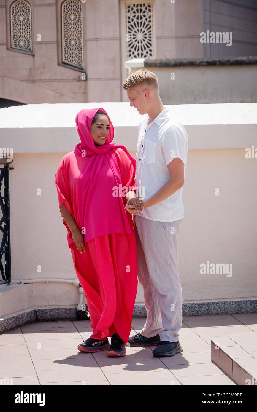 young muslim woman traditional vibrant pink hijab headscarf man smiling at each other mixed race relationship couple penang floating mosque malaysia Stock Photo