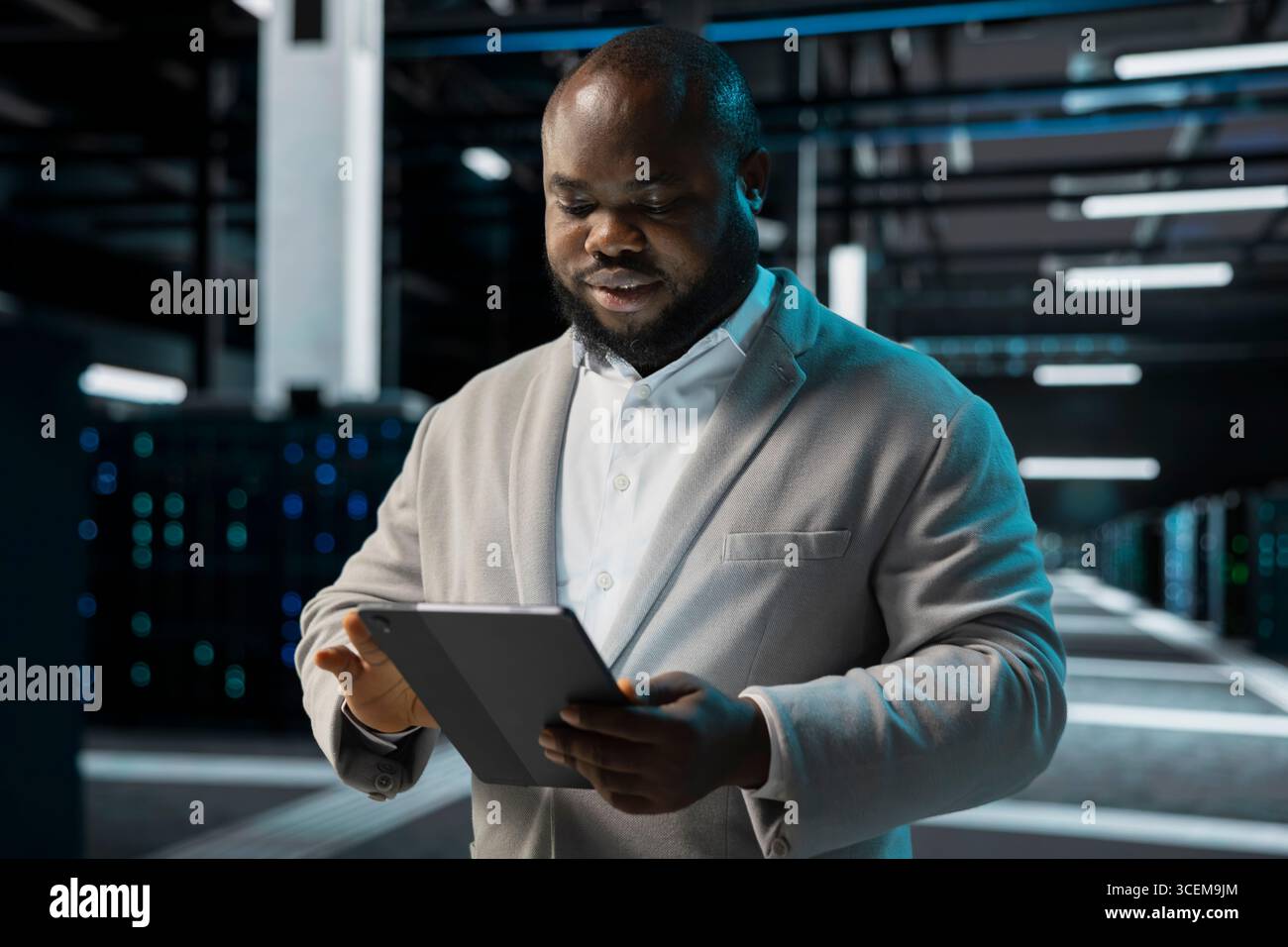 Engineer in server farm coordinating backups protocols, checking recovery plan. Data center IT specialist performing maintenance with tablet, making sure rigs are functioning optimally Stock Photo