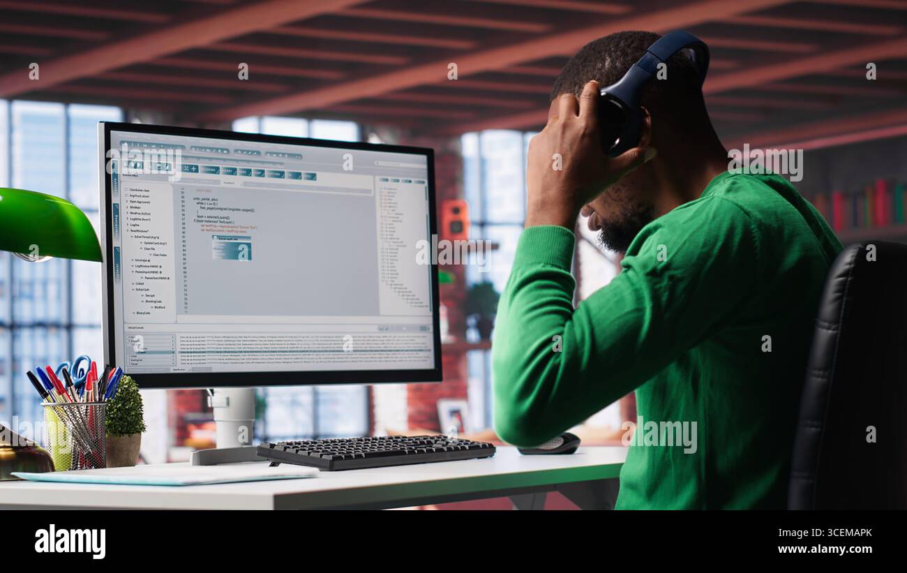 Tech savvy black engineer developing secure online program at home. Surrounded by binary data, freelancer works on interface design, script optimizations and network systems. Camera A. Stock Photo