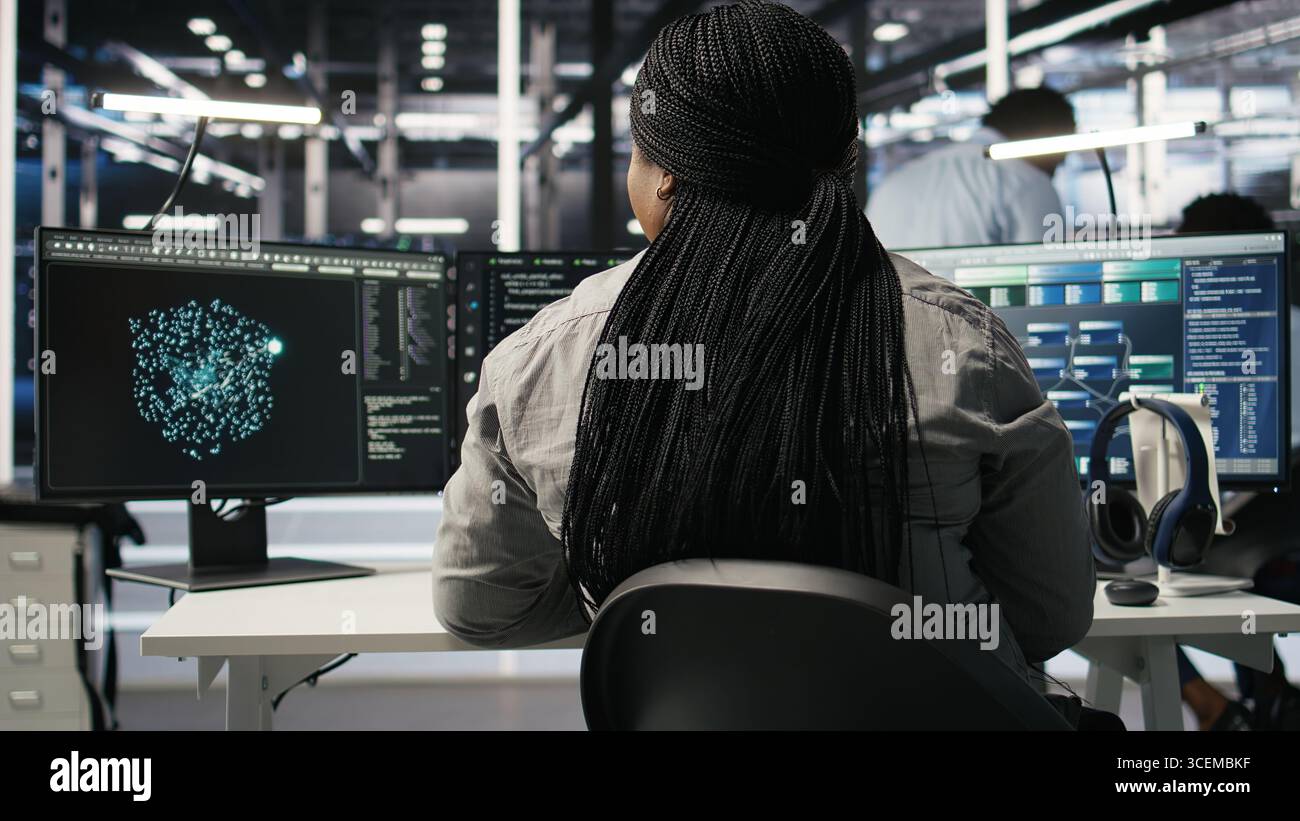 Data center admin does neural networks node tree programming, optimizing resource allocation. Server room IT professional uses predictive deep learning AI visualization systems, camera A Stock Photo