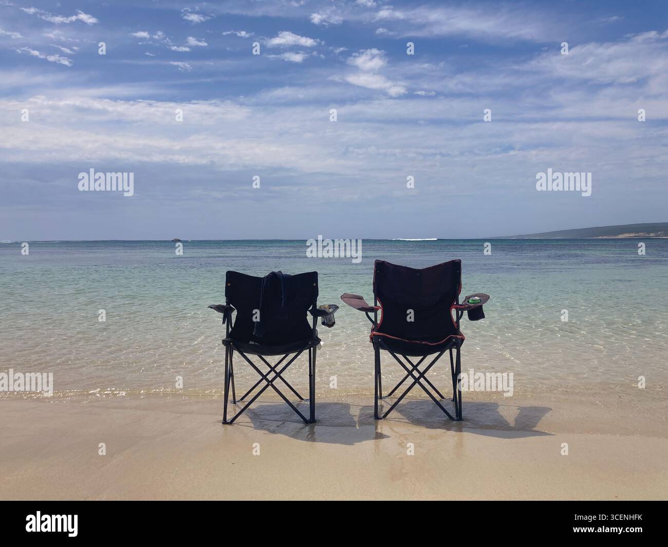 Two chairs facing the serene beach and ocean waves beneath a blue sky. - Smartphone Captured Stock Image
