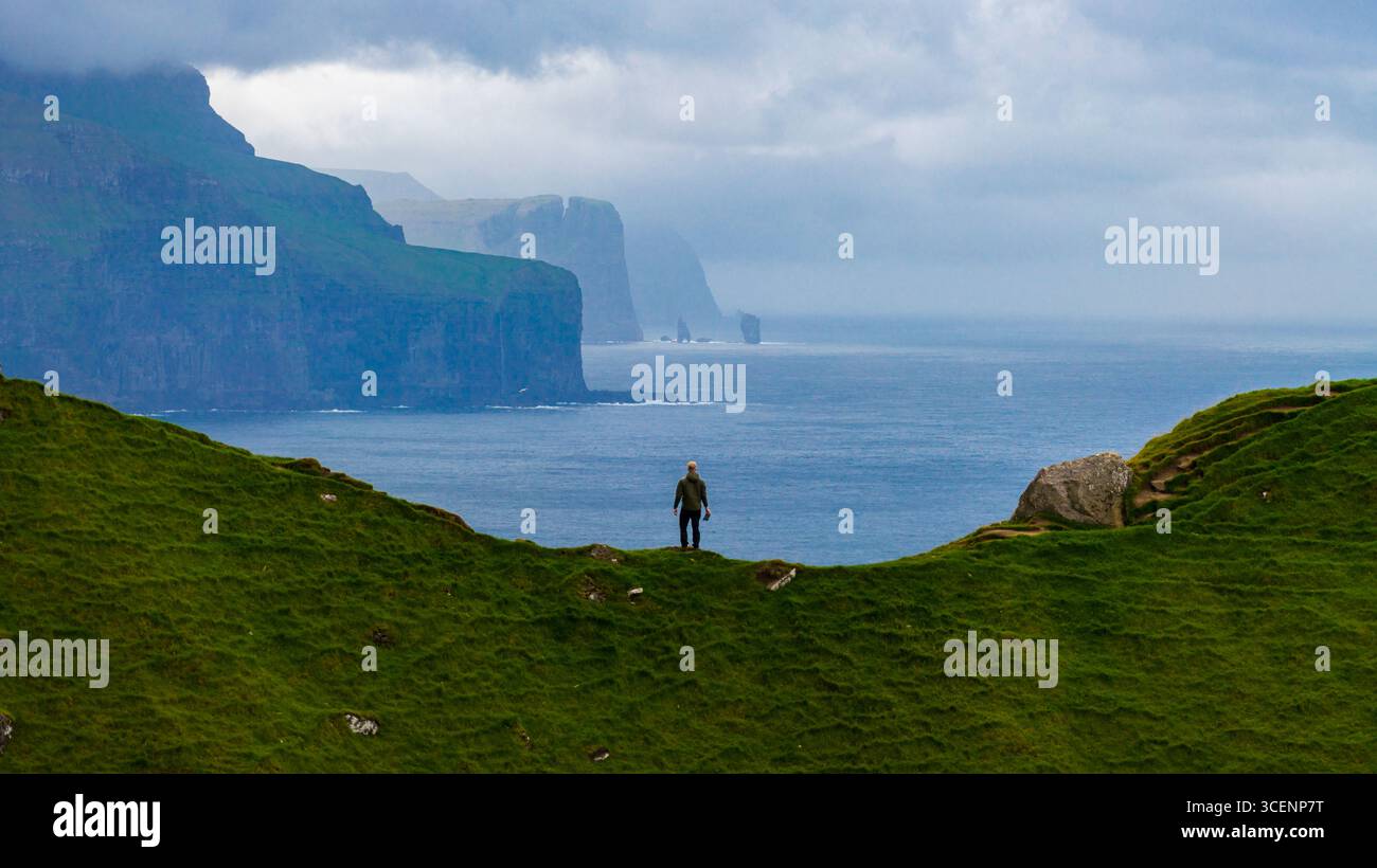 Aerial view of a solitary figure stands atop a vibrant green ridge ...