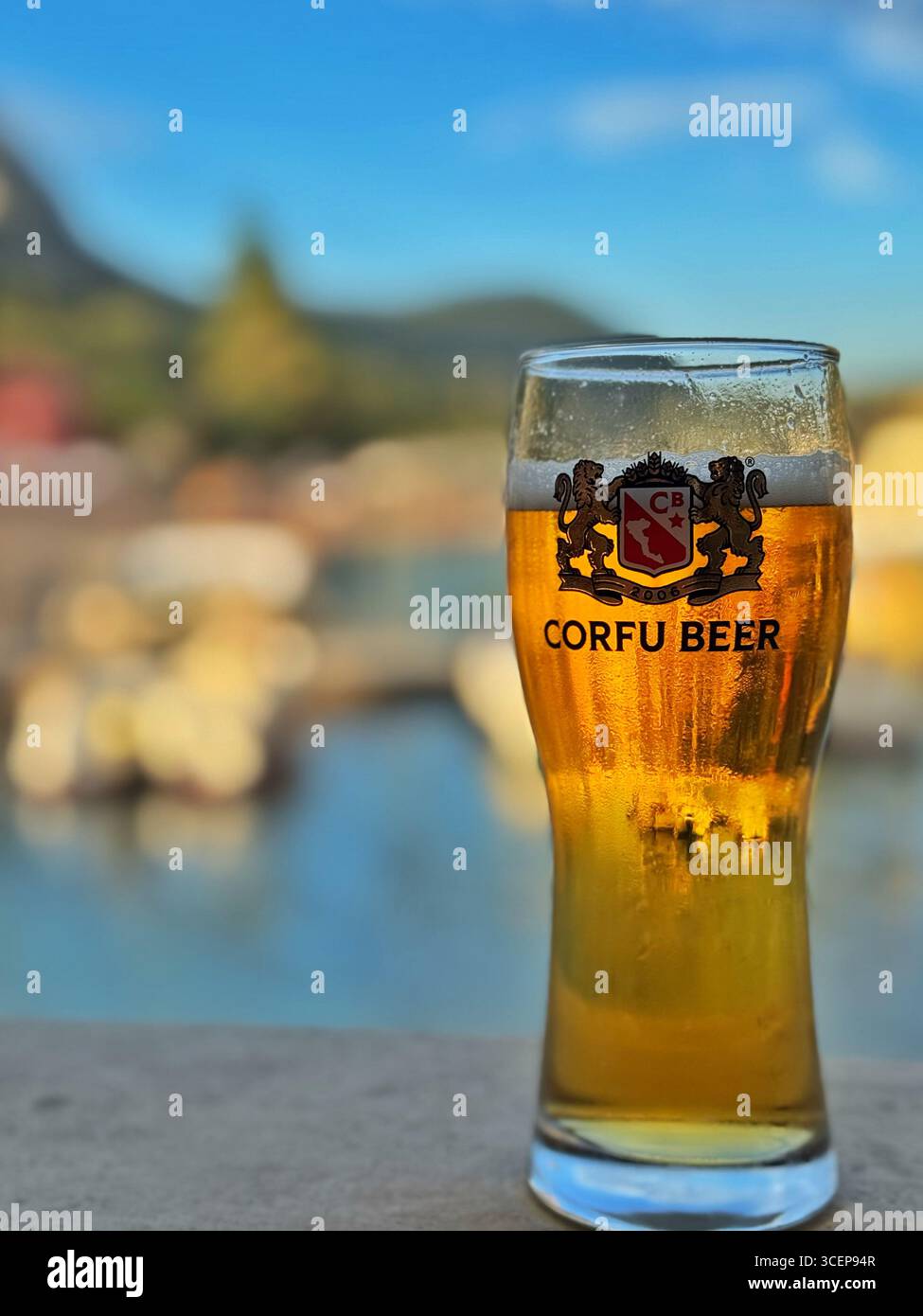 A glass of Corfu beer with Paleokastritsa beach behind, Corfu, Greece. - Smartphone Captured Stock Image